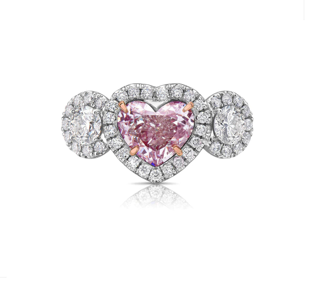 A heart-shaped light pink diamond ring with white diamond side stones set in a platinum band by Namdar